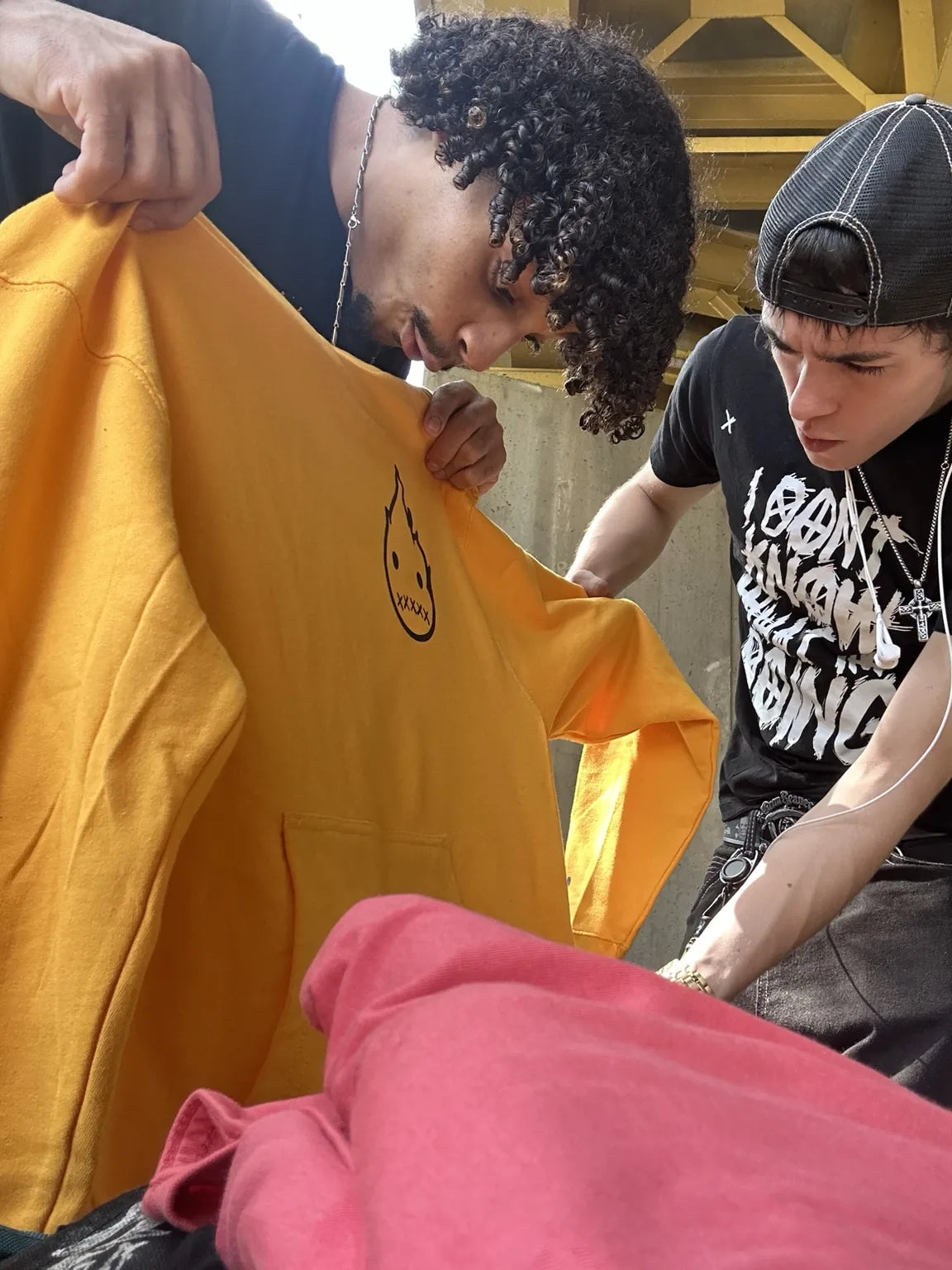 Two people looking over a yellow Rizo hoodie beneath a yellow-painted Pittsburgh structure