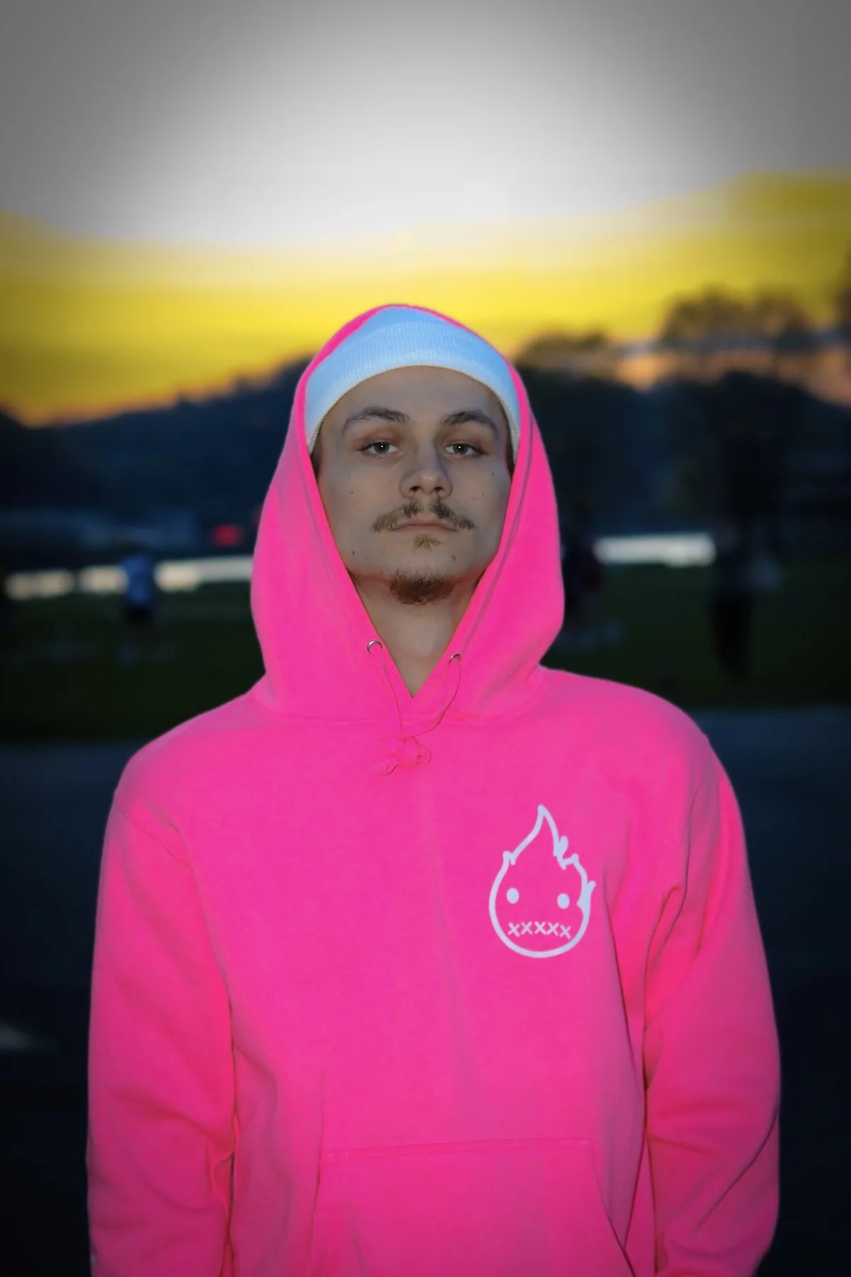 A person wearing a pink Rizo hoodie outdoors at sunset