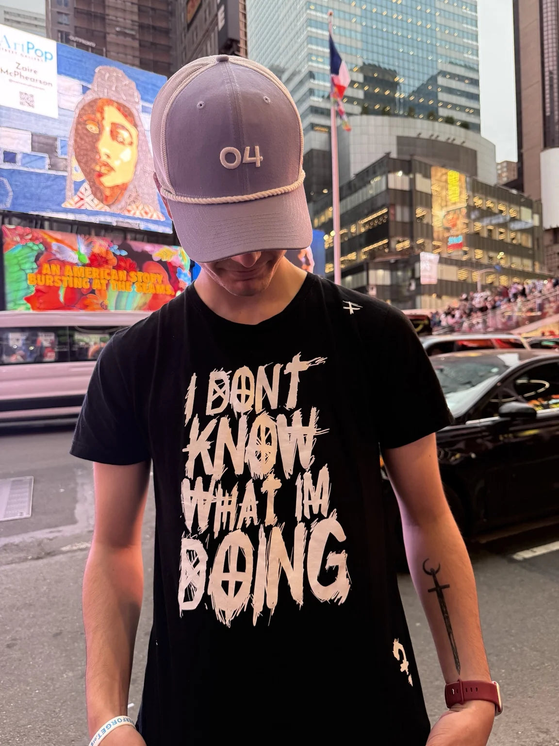 A person wearing a cap and black Rizo graphic T-shirt in Times Square
