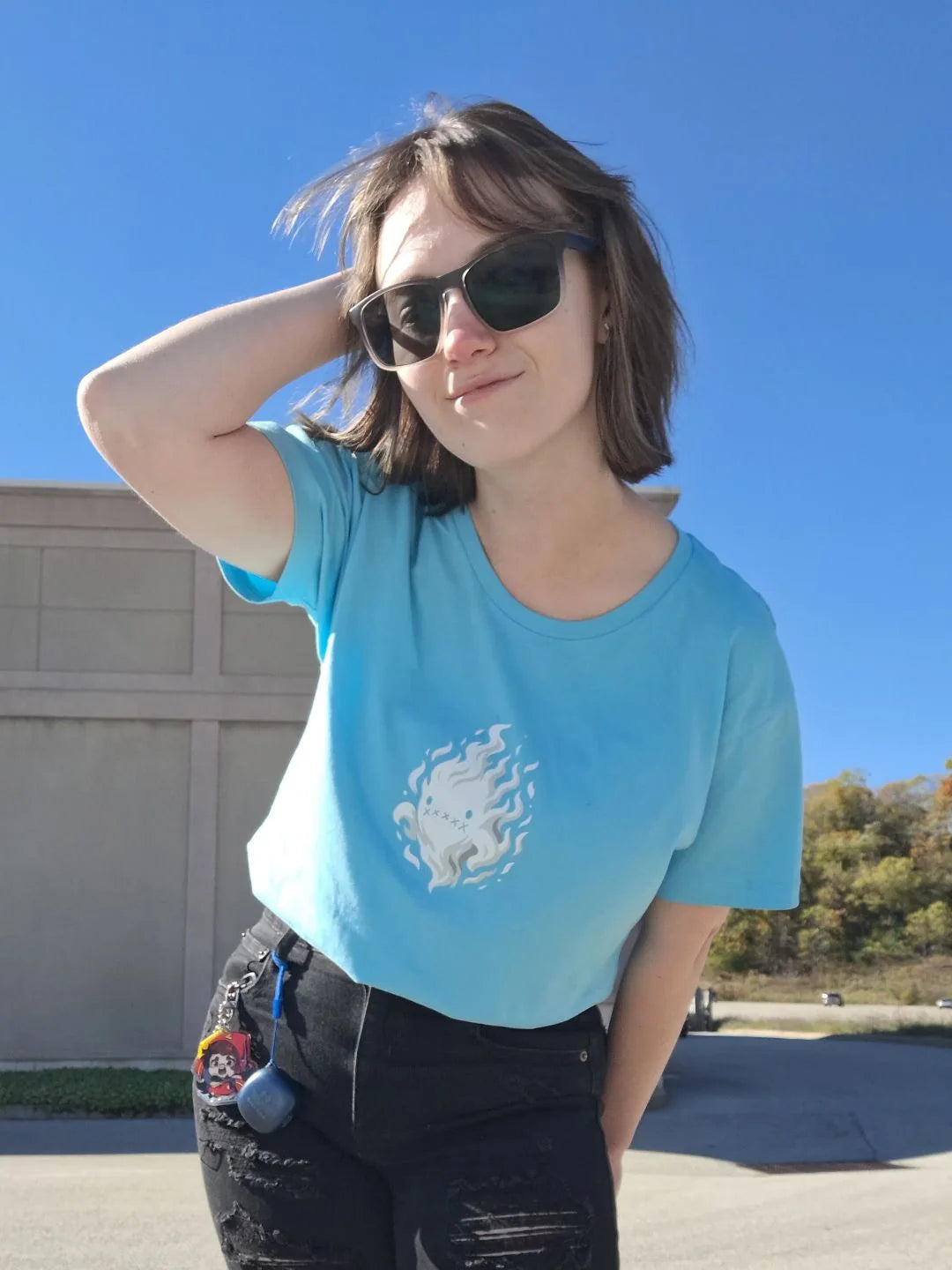 A person wearing sunglasses and a turquoise Rizo flame T-shirt outdoors under a clear blue sky